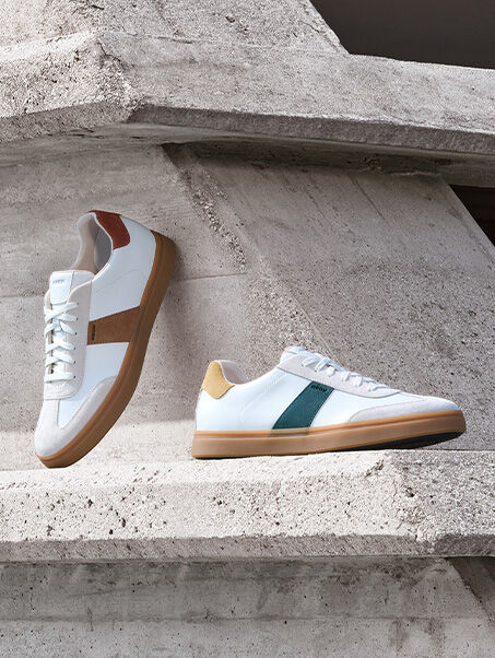 Man with his hand resting on a concrete block, balancing with one leg forward and one leg back, wearing two suede sneakers | GEOX | GEOX